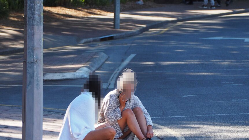 Two females sit on a curb.