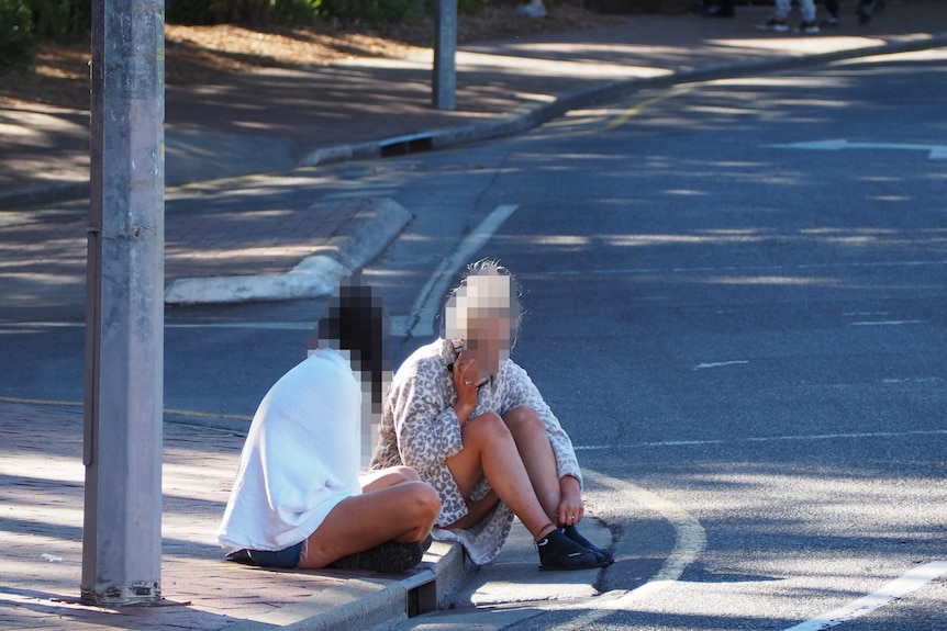Two females sit on a curb.