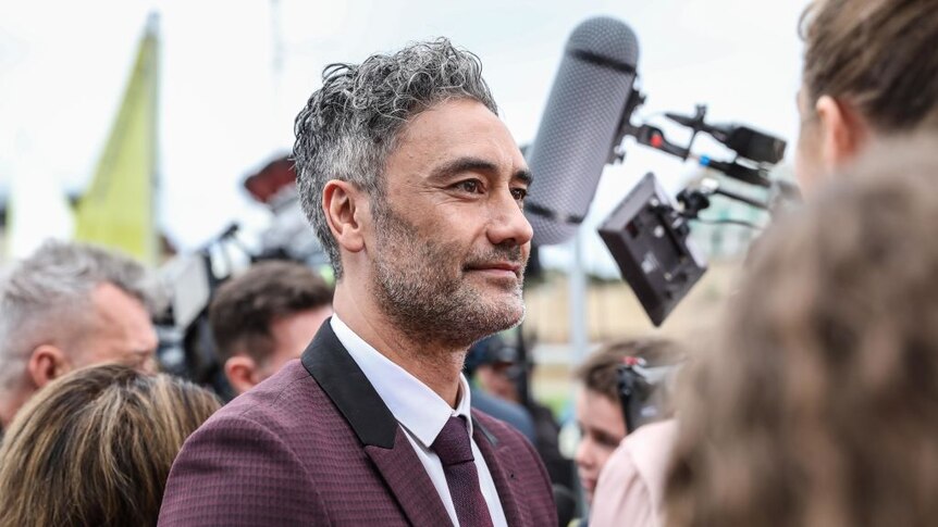 Director Taika Waititi stands in a crowd on the red carpet for a movie screening