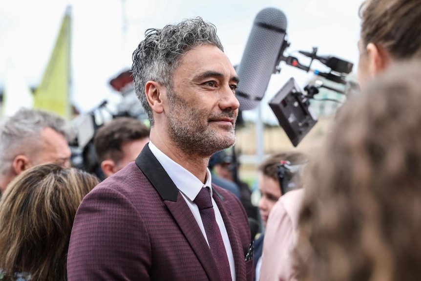 Director Taika Waititi stands in a crowd on the red carpet for a movie screening