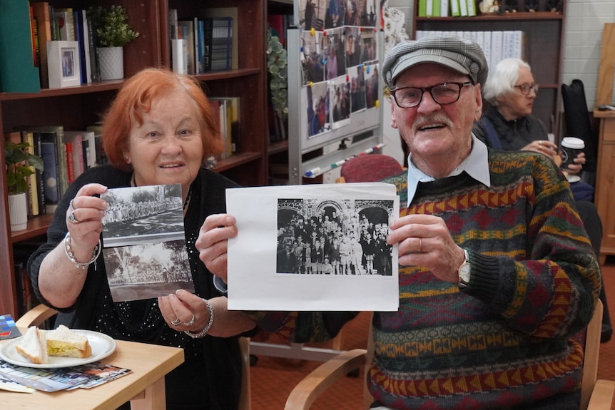 woman and man sit together holding up black and white photos
