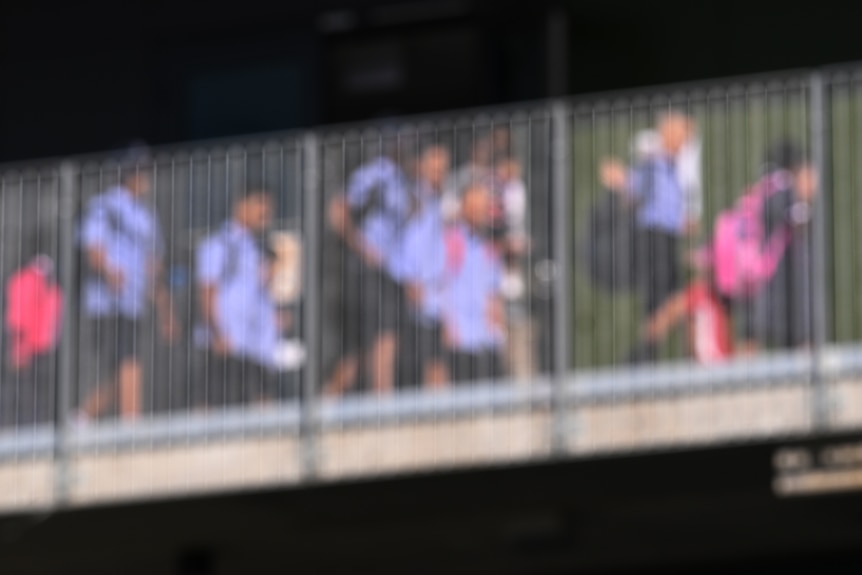 An out-of-focus photo of school children walking across a bridge from street view.