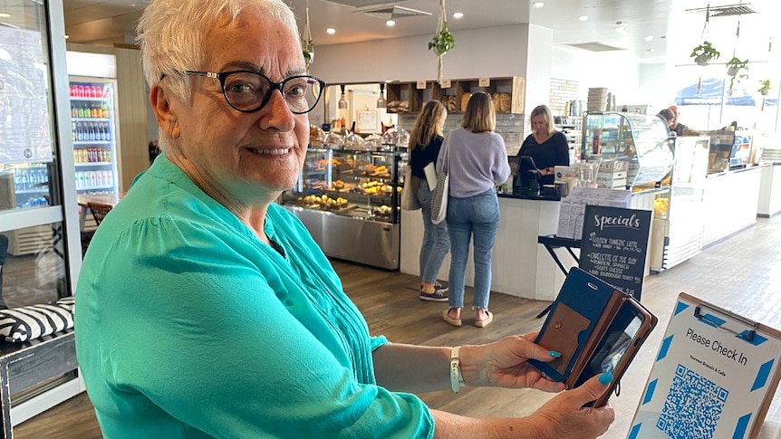 An older woman holds her phone towards a QR code on a stand at a cafe.