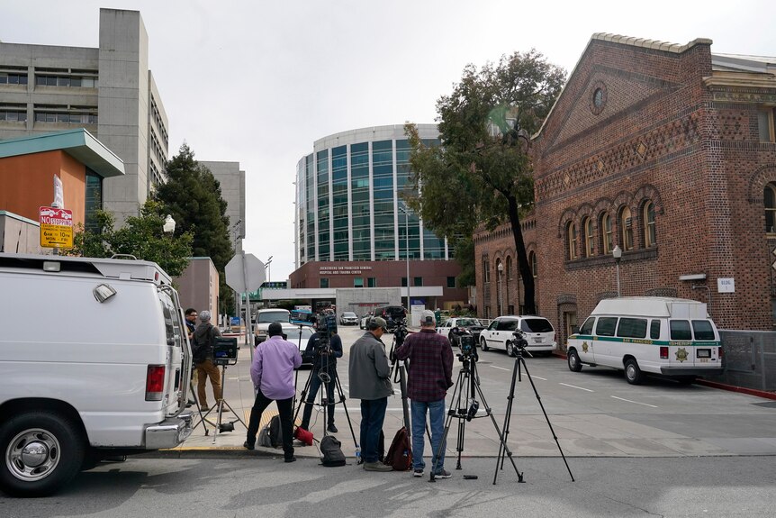 摄影师和摄影人员站在摄影机支架附近，这是一辆停在旧金山一家医院外的白色皮卡车