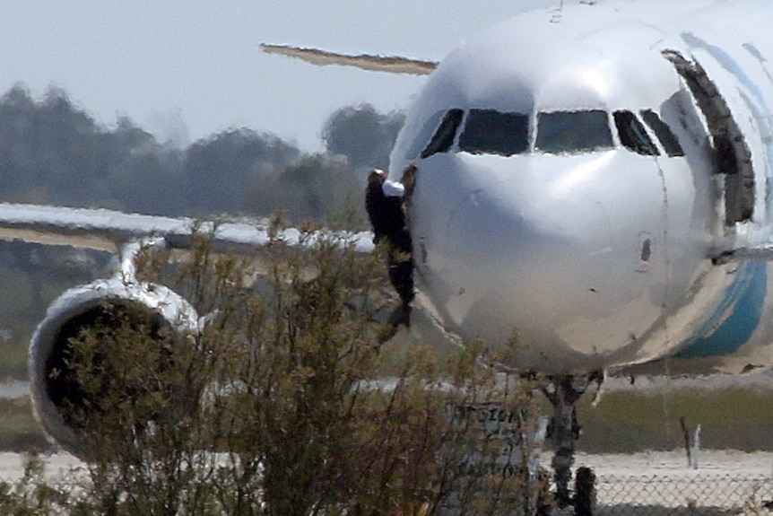 Man climbs out of plane window, hanging from cockpit