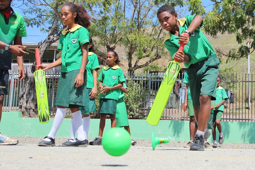 A young PNG boy in a green school uniform plays a straight drive at camera.
