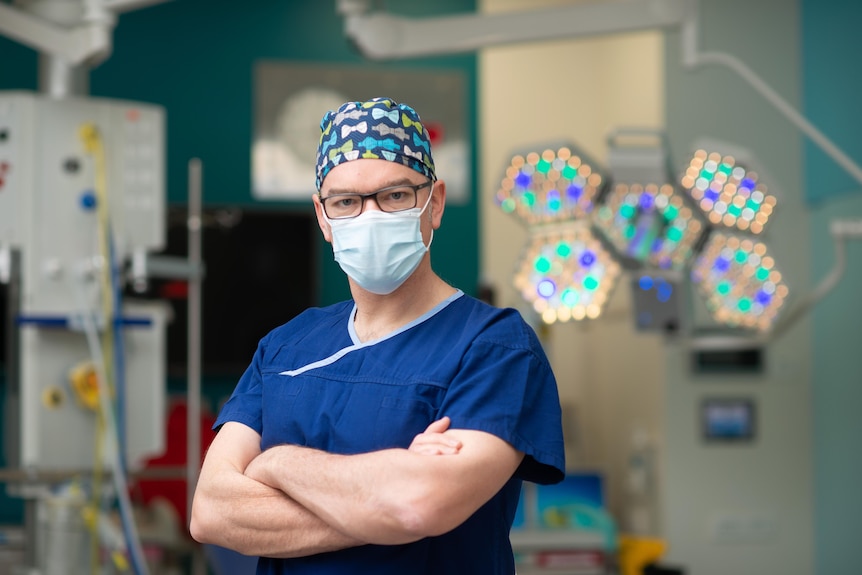 A man in scrubs and a mask standing in a hospital.