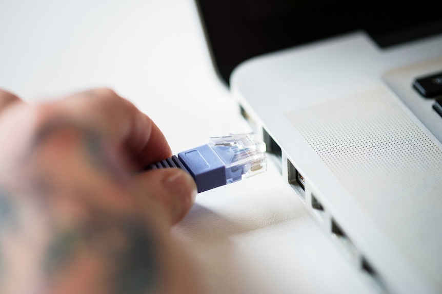 A LAN cable is held by a hand next to a laptop port.