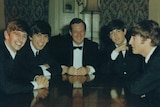 Five men in suits are sitting around a table talking and smiling