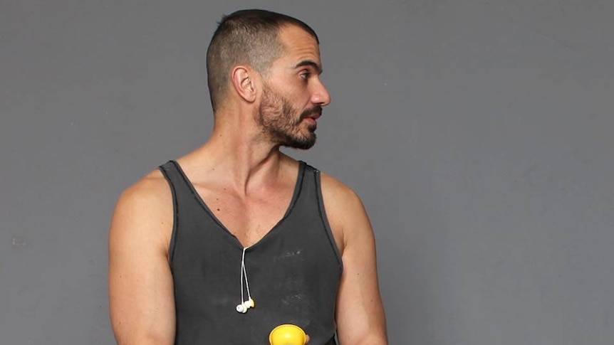 A bearded man wears a dark singlet with earphones hanging from the front.
