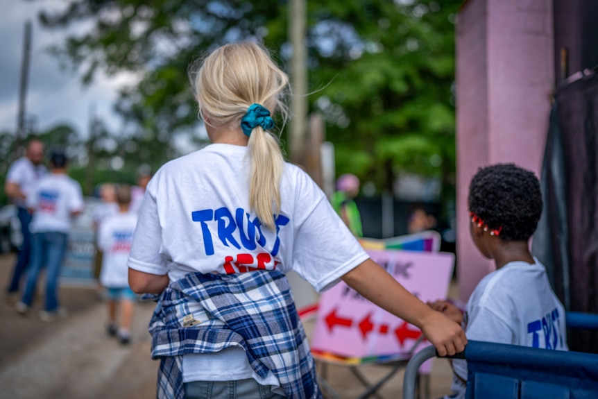 A little blond girl and a young African American child in shirts with "Trust Jesus" on the back