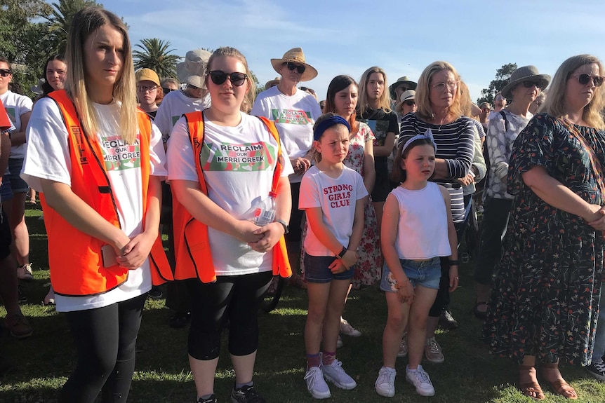 A crowd of people, mainly women, stand in a park. Some are wearing Reclaim Our Merri Creek shirts.