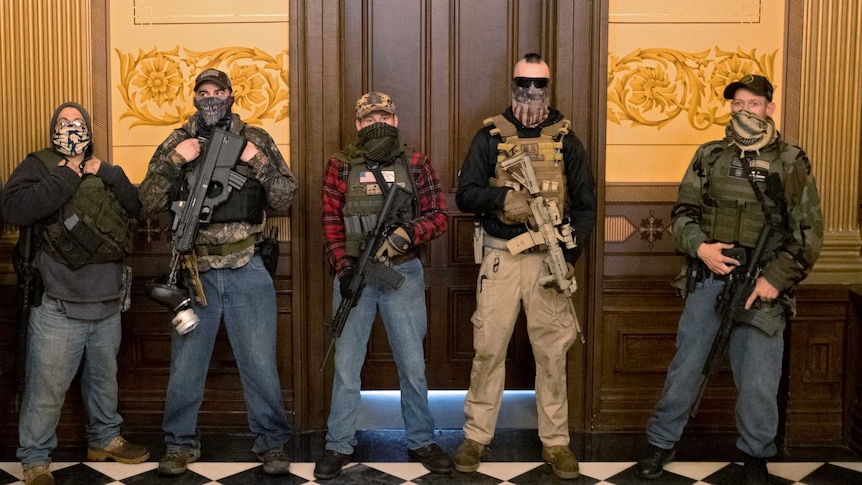 People in militia clothes with guns stand outside a door in a stately building