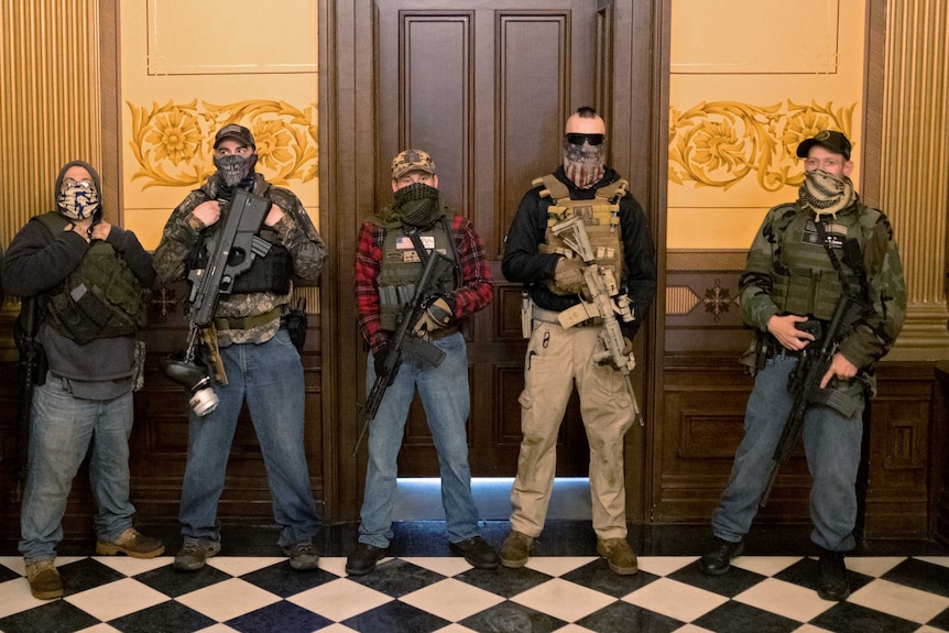 People in militia clothes with guns stand outside a door in a stately building