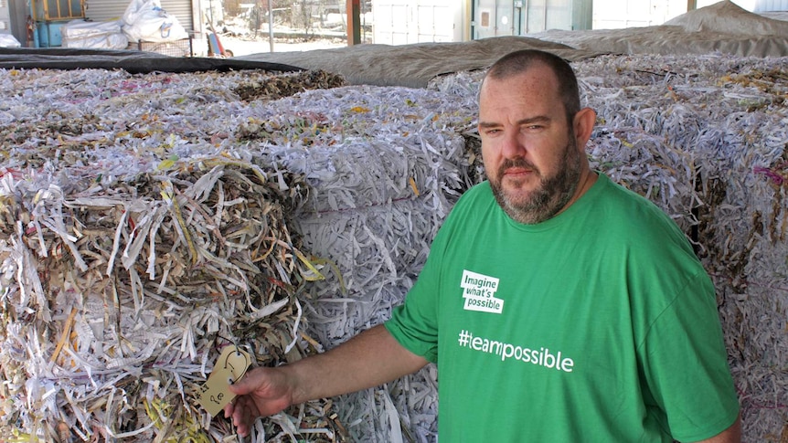 A man stands in front of giant bales of shredded paper.