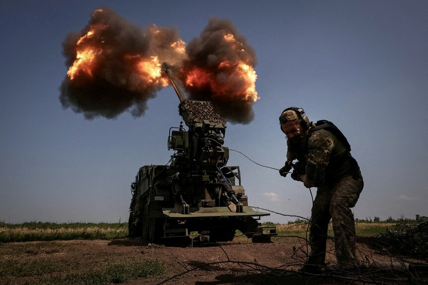A soldier pulls a cord to fire a howitzer.