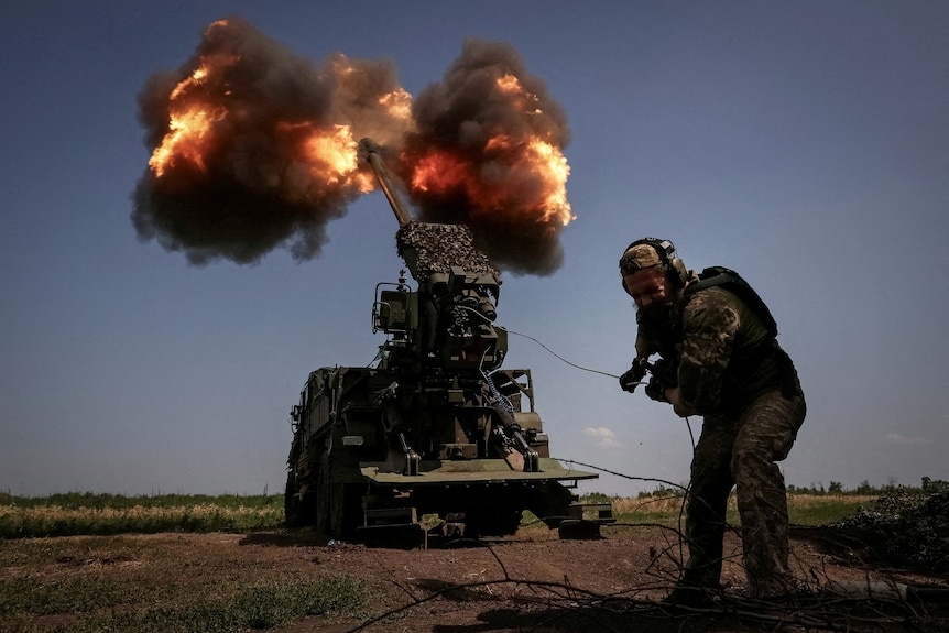A soldier pulls a cord to fire a howitzer.