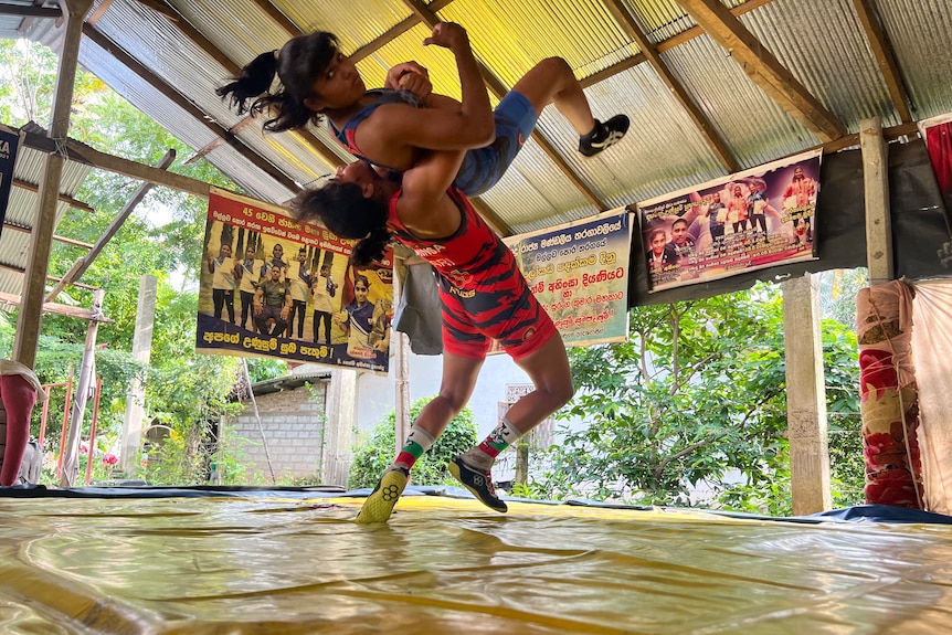 Two women wrestlers are training. One has lifted the other in the air and is preparing to bodyslam.