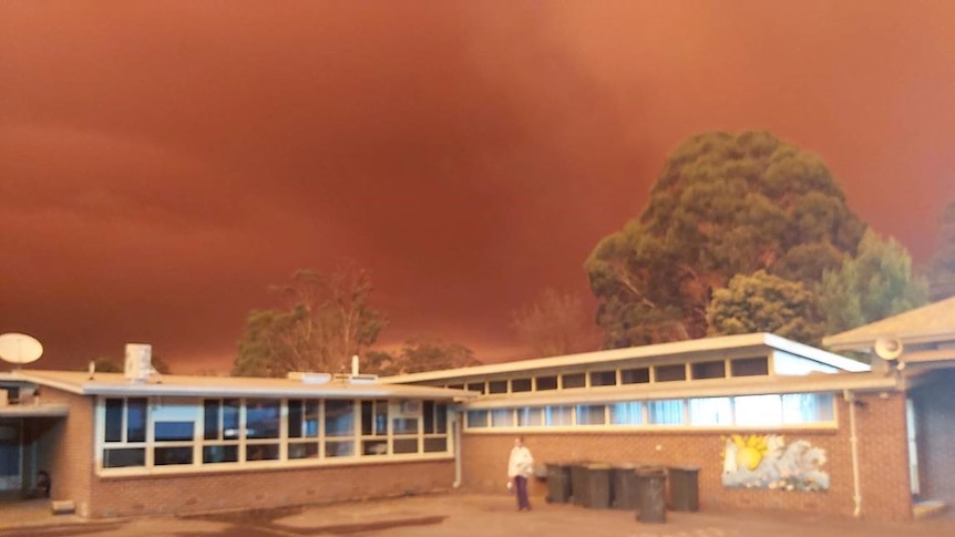 A dark red sky hangs over a small school building.