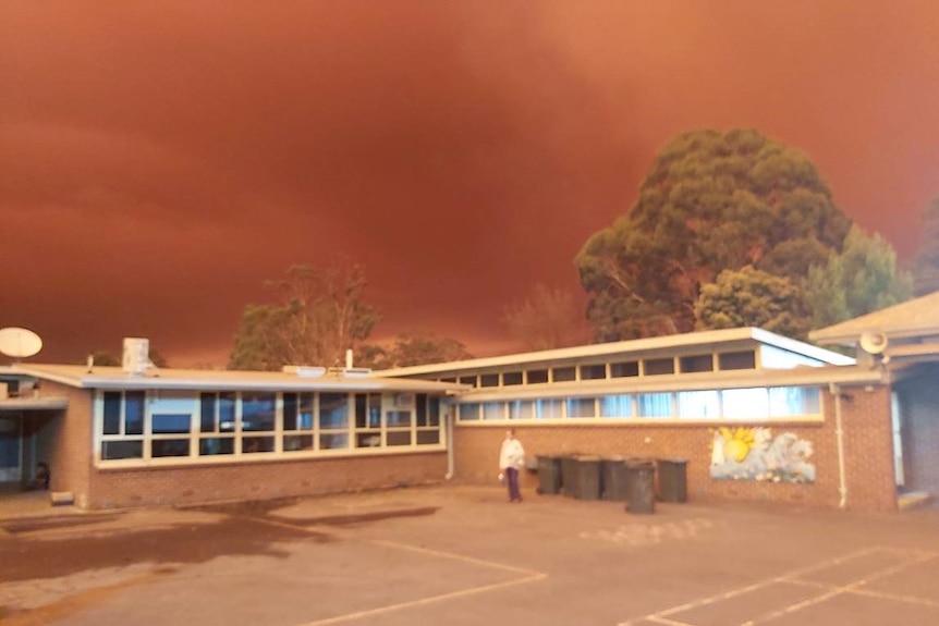 A dark red sky hangs over a small school building.