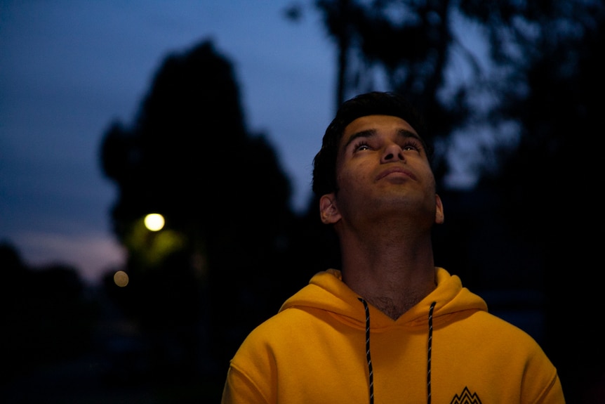 A young man in a yellow jumper looks up into the night sky
