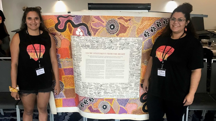 Photo showing Allira Davis & Bridget Cama from Uluru Youth Dialogue standing next to copy of Uluru Statement from the Heart.