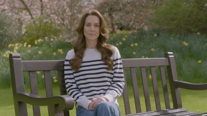 A woman with long brown hair sits on a wood bench