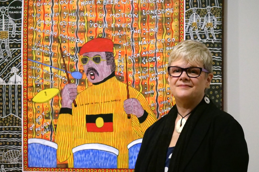 A woman poses in front of a painting by First Nations artist Robert Campbell Junior.