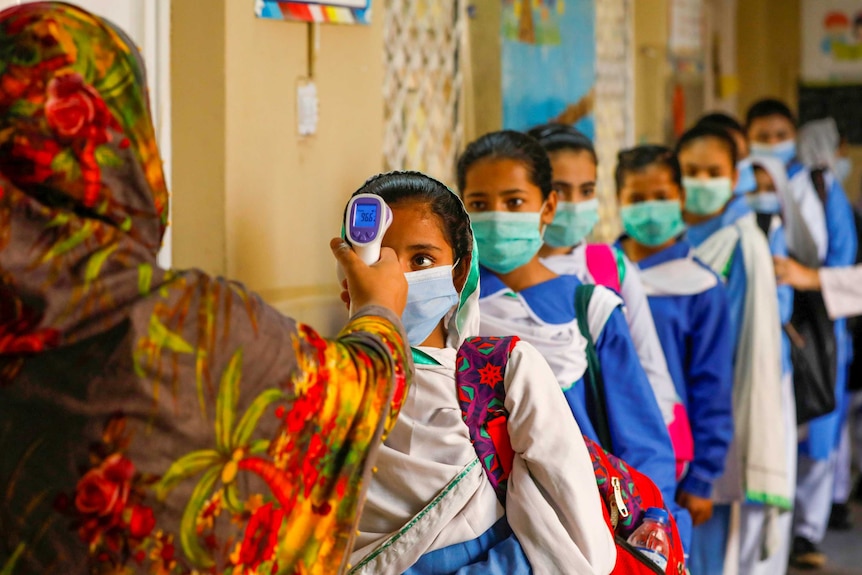 A row of little girls in face masks getting their temperature checked