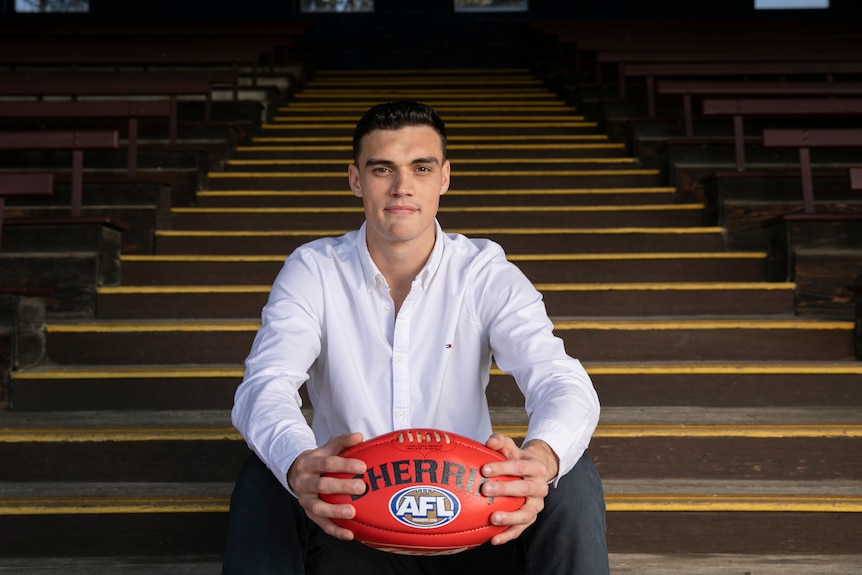 Patrick Bines holding a footy, sitting on stairs.