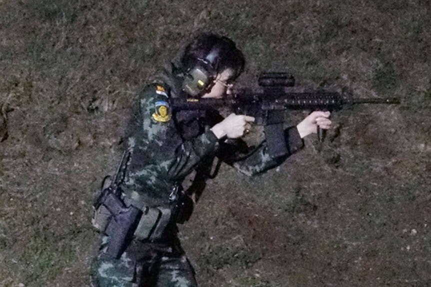 Consort Sineenat Wongvajirapakdi in military fatigues, aiming and firing a gun