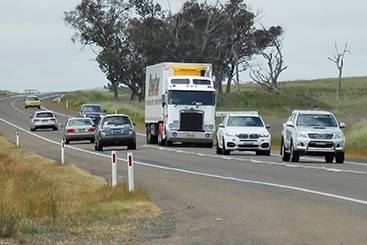 A large truck drives down a country highway, surrounded by smaller vehicles.