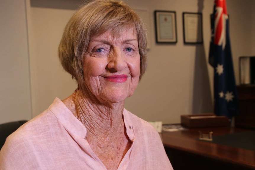 A lady with short hair and a pink shirt smiles at the camera