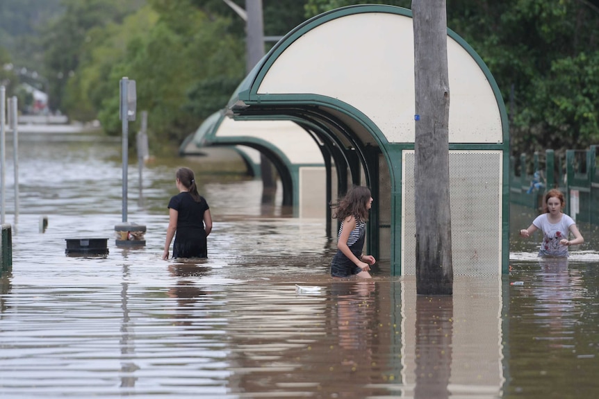 Girls walk through hip-deep floodwaters as they recede in Lismore on Sunday morning.
