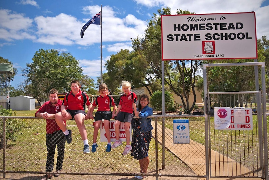 The students and staff of Homestead State School at the front gate, the students are sitting on the fence