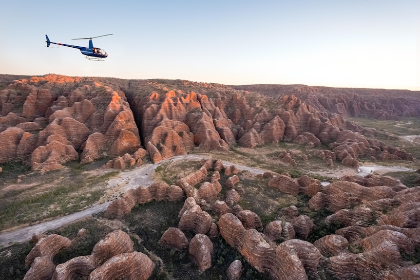 helicopter flies above beehive-like  rock formations 