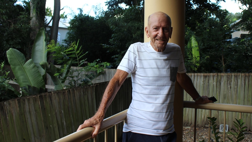 A smiling elderly man on a patio with trees behind him