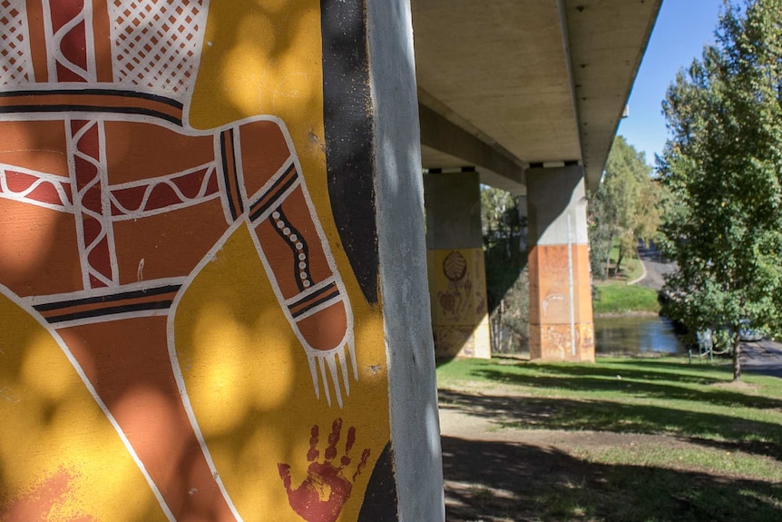 Murals with aboriginal designs on pylons under a bridge near a river