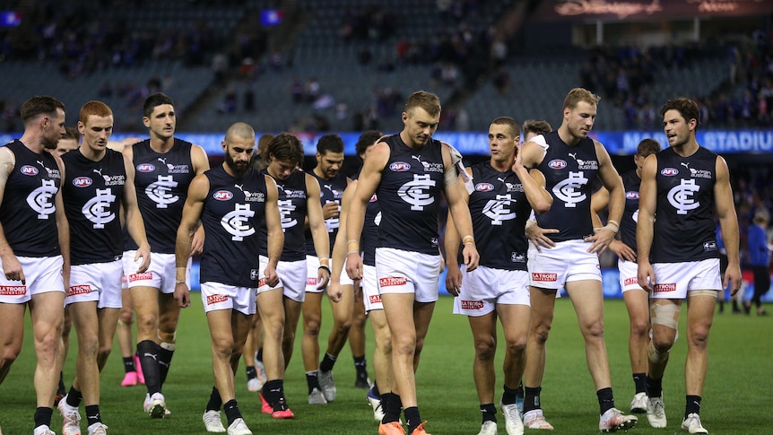 A dejected group of AFL players walk off the ground after a loss.