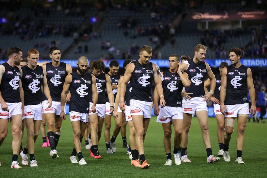 A dejected group of AFL players walk off the ground after a loss.