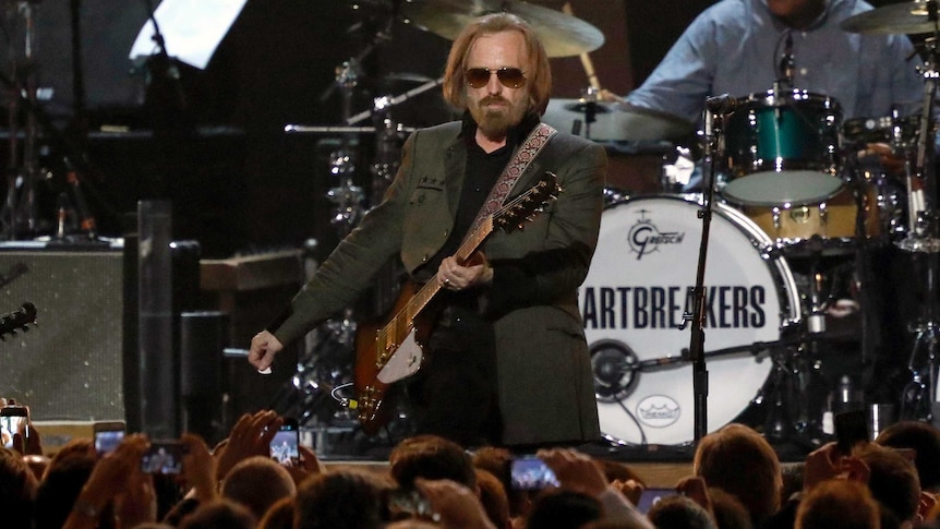Musician Tom Petty strums his guitar on stage in front of hundreds of fans.