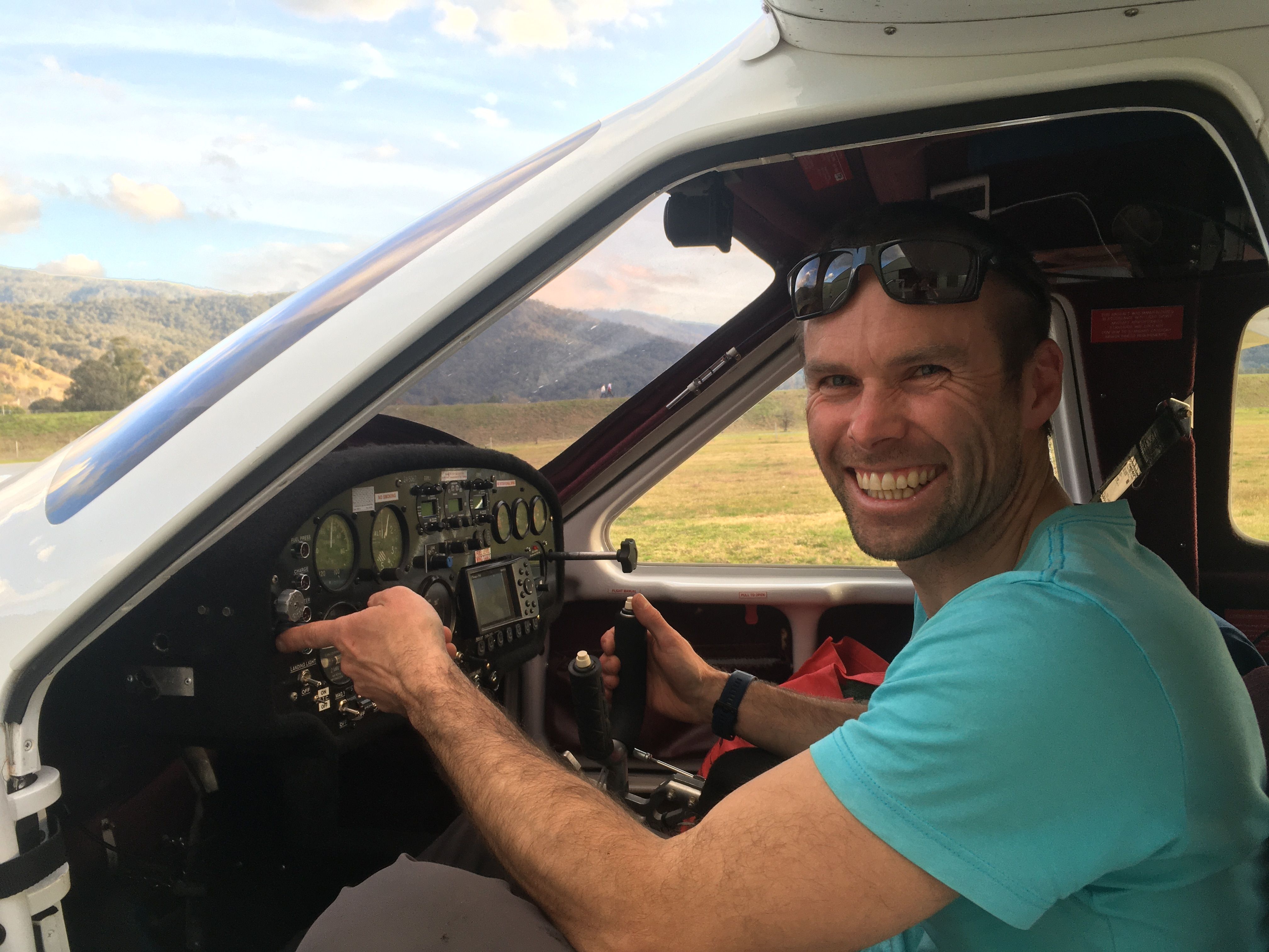 Matthew Farrell smiles looking at the camera while sitting in the cockpit of a small aeroplane.