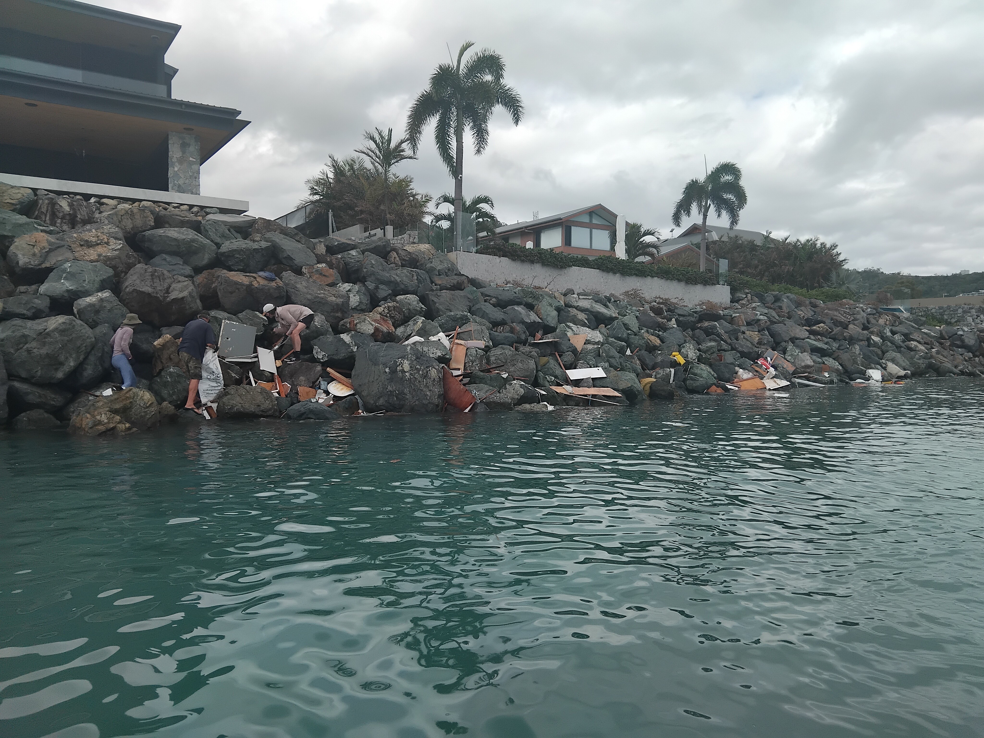 Un grupo de personas trepa por las rocas para recoger trozos de madera y muebles rotos atrapados en la pared rocosa.