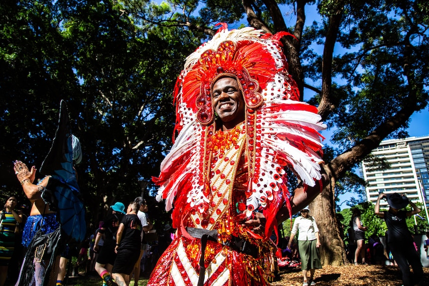 Un homme, vêtu d'une tenue ornée de plumes rouges, pose pour la caméra