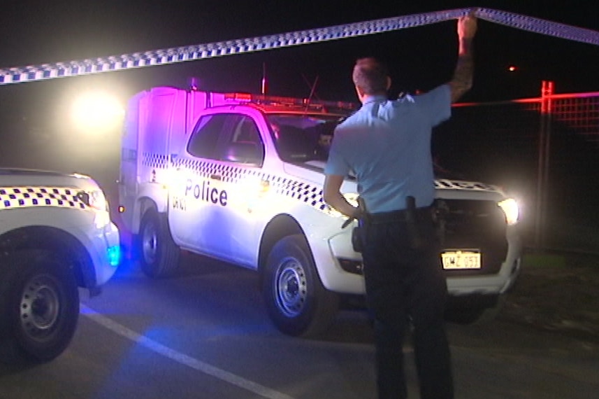 A WA Police paddy wagon drivers under police tape lifted up by an officer at a cordon at night.