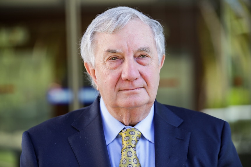 A man with grey hair wearing a suit looking serious.