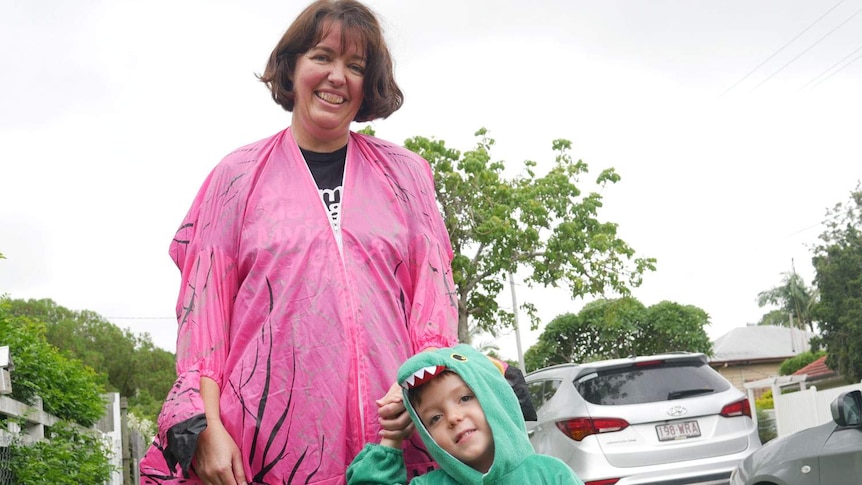 Lou Bromley and her four-year-old son Angus Love, wearing dinosaurs costumes, stand on the footpath.