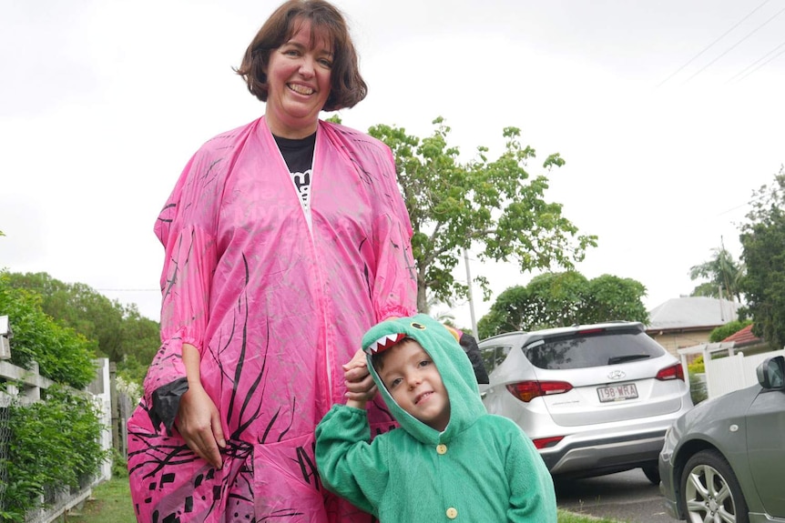 Lou Bromley and her four-year-old son Angus Love, wearing dinosaurs costumes, stand on the footpath.
