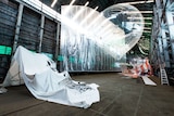 An installing of a giant clear plastic balloon, hanging reflective plastic sheeting among other things inside a warehouse space.