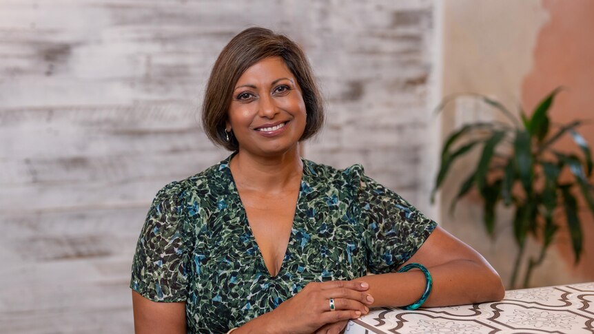 Broadcaster and Compass host Indira Naidoo sitting at a table smiling 